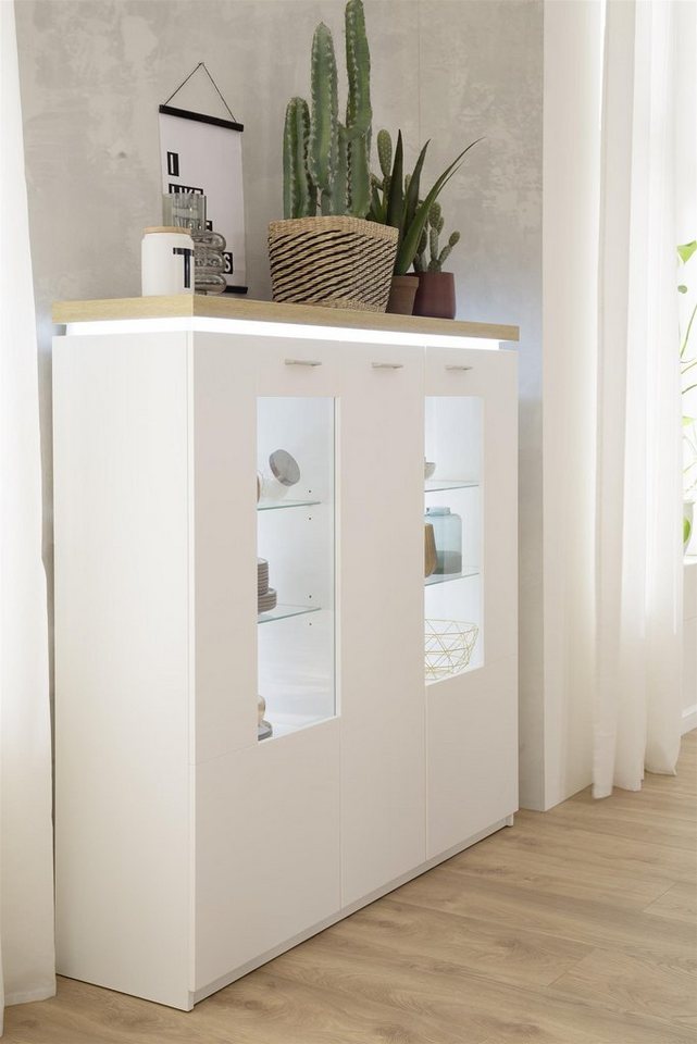 möbelando Highboard Chalki, Modernes Highboard aus melaminbeschichteter Spanplatte in Weiß, Deckplatte und sichtbare Rückwand in Wotan Eiche Nachbildung mit 2 Glas-/Holztüren, 1 Holztür, 4 Glaseinlegeböden, 4 Konstruktionsböden und 1 Einlegeboden, inkl. Deckplattenbeleuchtung. Breite 138 cm, Höhe 143 cm, Tiefe 38 cm von möbelando